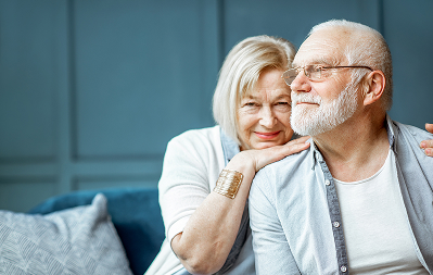 Elderly couple smiling, embracing on a sofa.